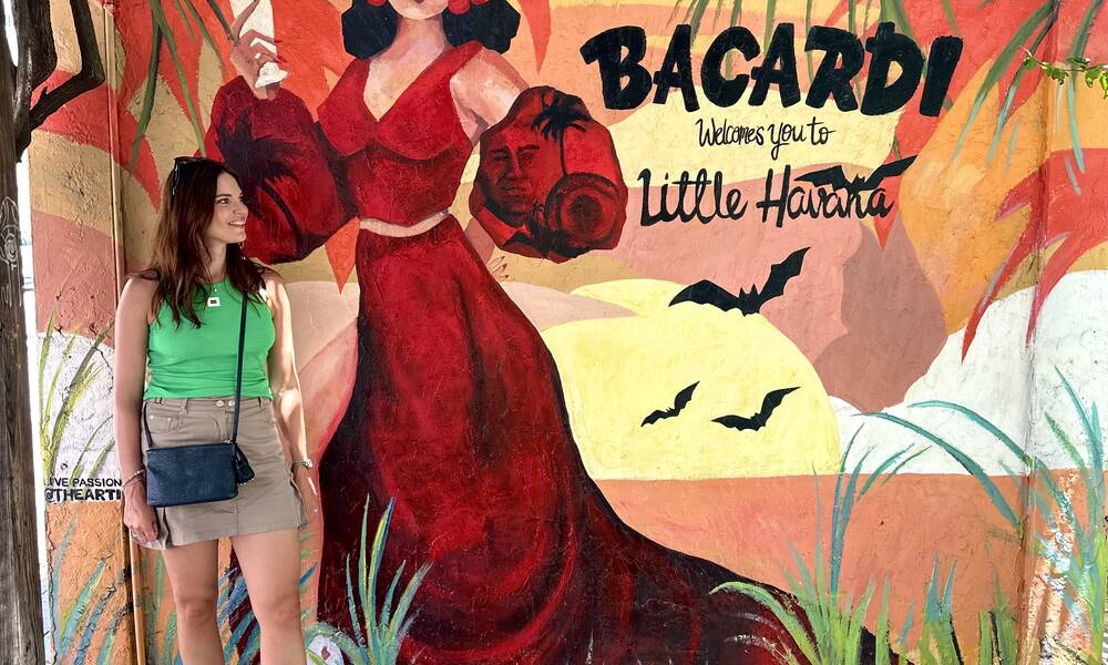 Carola staat voor een rode muurschildering. Hier wordt een vrouw in rode jurk op afgebeeld met de tekst Bacardi welkcomes you to Little Havana